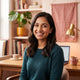 A smiling South Asian woman looking towards the camera, representing a happy customer in a warm, modern home environment.